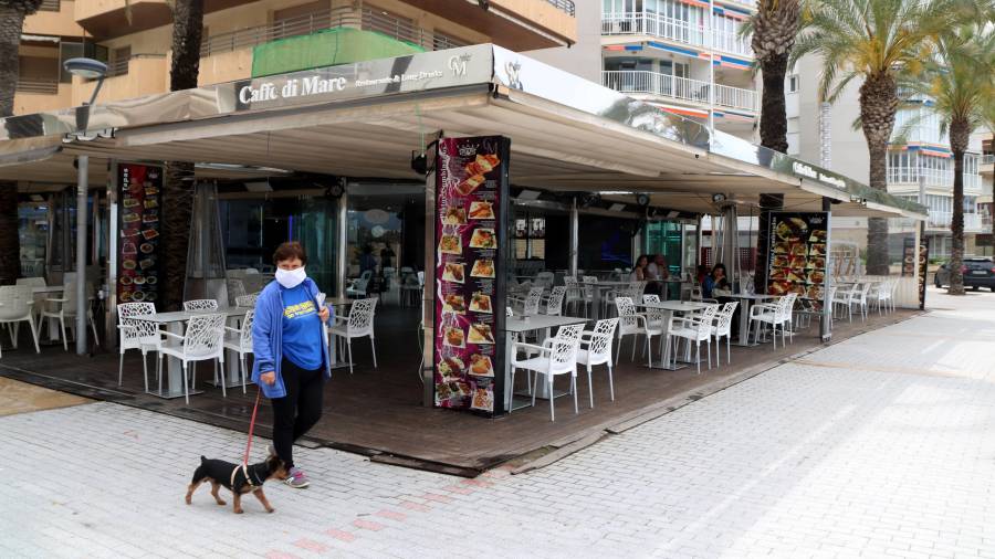 Plan abierto de una mujer paseando un perro borde una terraza del paseo de Salou prácticamente sin clientes el 25 de mayo de 2020. Foto: ACN