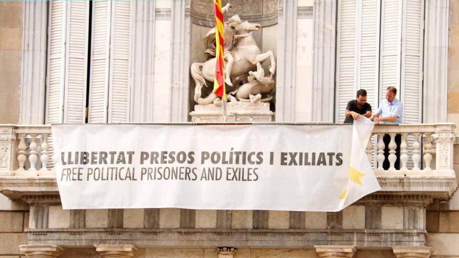 Dos trabajadores de la Generalitat descuelgan del balcón la pancarta que pide la libertad de los presos.