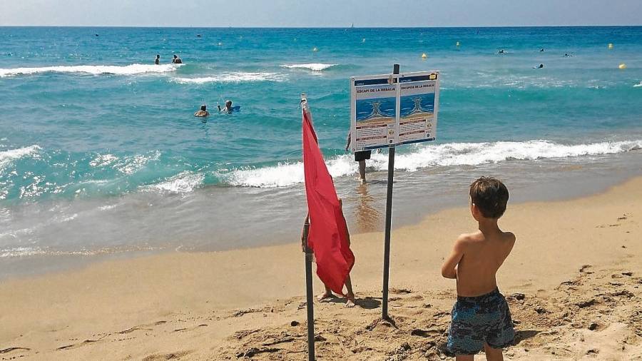 Un niño lee la información sobre las resacas junto a la bandera roja en la orilla. FOTO: JMB