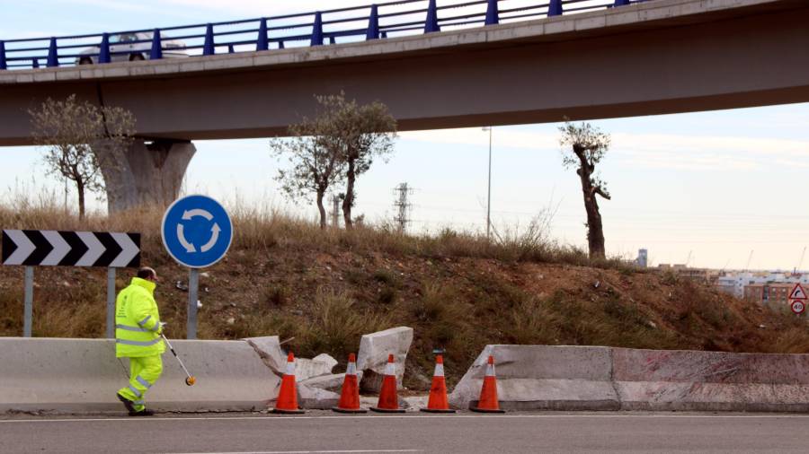 Un operario de carreteras tomando medidas en la rotonda del T-11, en Tarragona, donde se produjo el accidente, con la valla destrozada a su lado.