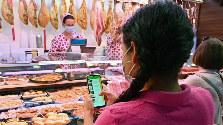Imatge d’una parada del Mercat Central i una persona que fa servir l’aplicatiu mòbil de compra en línia del segell Ulabox. FOTO: ALFREDO GONZÁLEZ.