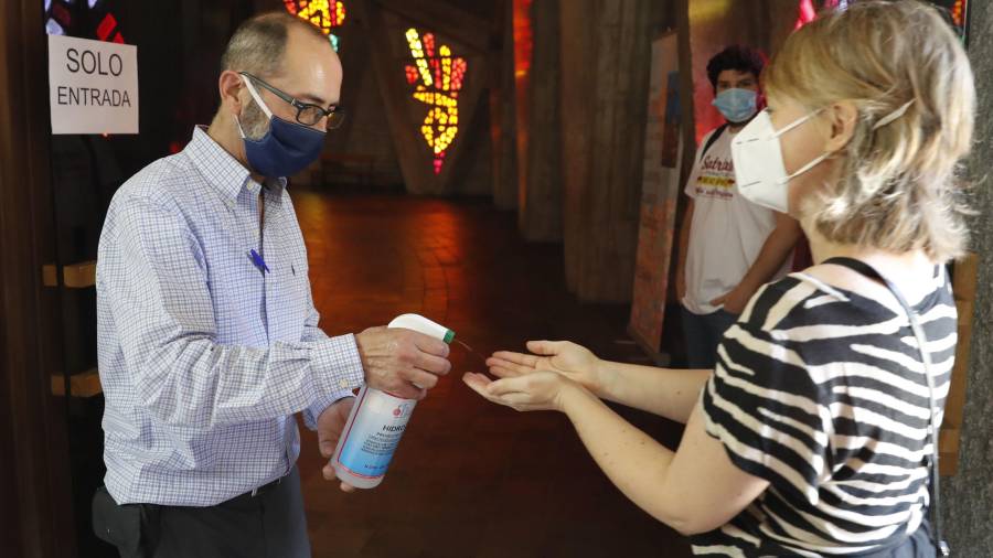 Un hombre echa gel hidroalcohólico en las manos de una mujer antes de entrar en una iglesia. FOTO: EFE