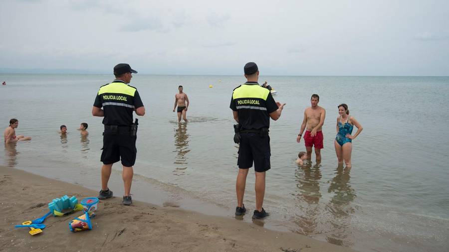 Dos agentes piden a los bañistas que salgan de la playa ante la presencia de dos ejemplares de pez raya. FOTO: Joan Revillas